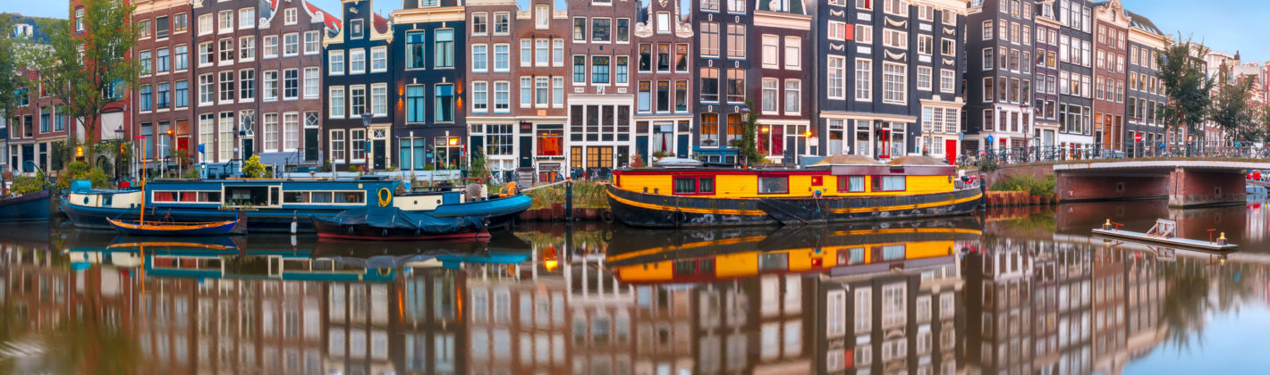 Panorama of Amsterdam canal Singel with typical dutch houses and houseboats during morning blue hour, Holland, Netherlands.